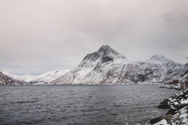 Norveç 'in Senja adasındaki ıssız Husoy köyünden görüntü. Çok yalnız bir balıkçı köyü. Fırtınalı Norveç denizi ve Kuzey Kutbu 'nun ötesindeki karlı tepelerin manzarası.