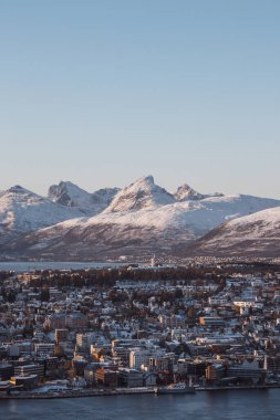 Kuzey Norveç 'teki Tromso' nun kutup kasabası ve günbatımında arka plandaki karlı tepeler. Turuncu kırmızı çizgiler kayalık dağlar. Dünyayı keşfetmek. Bir İskandinav şehri ve doğanın güzelliği.
