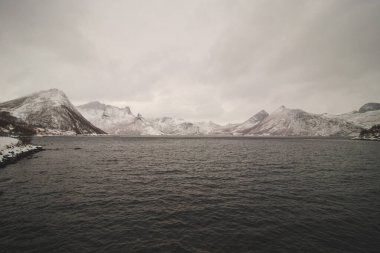 Norveç 'in Senja adasındaki ıssız Husoy köyünden görüntü. Çok yalnız bir balıkçı köyü. Fırtınalı Norveç denizi ve Kuzey Kutbu 'nun ötesindeki karlı tepelerin manzarası.