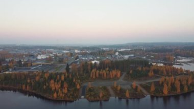 Oulujarvi Gölü ve Finlandiya 'nın orta kesimindeki Kajaani çevresindeki sonbahar ormanlarının insansız hava aracı görüntüleri. Turuncuya boyanmış yaprak döken orman çevresindeki insansız hava aracı görüntüleri. Gün batımı. 4k video