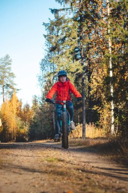 Hoş, gerçekçi bir gülümsemesi olan genç bir bayan eğlence olsun diye spor yapıyor. Fin vahşi doğasında şişman bisikleti süren bisikletçi. Vuokatti bölgesi. Bisiklet kıyafeti ve kask. Döngü.