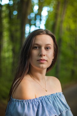 Güzel bir yaz mavi elbisesi içinde, gür yaz ağaçlarıyla çevrili bir orman yolunda genç bir esmerin nefes kesici samimi portresi. Ölçülü ve hırslı bir bakış..
