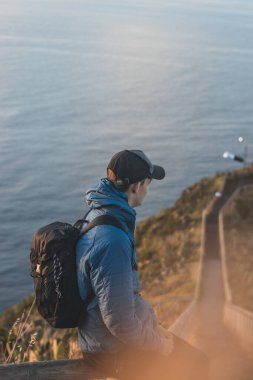 Ceket giyen öğrenci, Cristo Rei, Camara de Lomos, Madeira 'nın Portekiz' e ait manzarasının keyfini çıkarıyor. Atlantik kıyısında gün doğumu. Avrupa kıtasının keşfi.