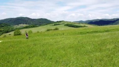 Kahverengi saçlı sporcu kasıklarını esnetir ve güneşli bir havada tepenin tepesinde yan hamlelerle vücudunun alt kısmını çalıştırır. 4k video
