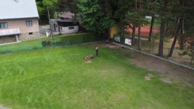 Açık hava müdürü büyük turnuvaya hazırlanmak için uzun taze çimleri biçiyor. Orta yaşlı bir adam çim biçme makinesiyle çimleri kesiyor. İHA atışı. 4k video