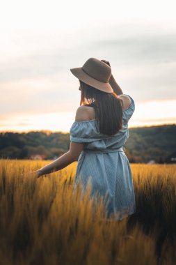 20-24 yaşlarındaki esmer bir kadının nefes kesici samimi portresi mısır tarlasında güzel mavi bir elbise ve şapkayla doğal bir şekilde gülümsüyor. Moda klasiği. Kahverengi saçlı Avrupalı bir kadının doğal güzelliği..