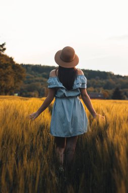 20-24 yaşlarındaki esmer bir kadının nefes kesici samimi portresi mısır tarlasında güzel mavi bir elbise ve şapkayla doğal bir şekilde gülümsüyor. Moda klasiği. Kahverengi saçlı Avrupalı bir kadının doğal güzelliği..