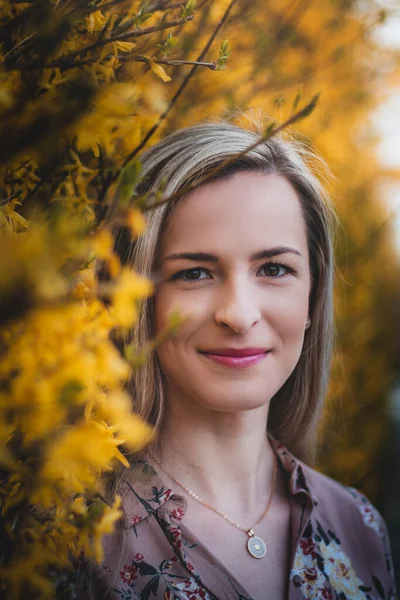 Güneşli bir yaz gününde çiçek açan ağaçların altında genç bir bayanın doğal gülümsemesi. Gerçek insanlar. Yazlık elbise giymiş sarışının samimi portresi. Pembe ve sarıların karşıtlığı.