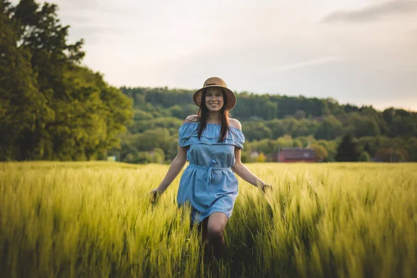 Breathtaking candid portrait of a brunette aged 20-24 walks in a beautiful blue dress and hat in a cornfield, smiling naturally. Fashion vintage style. Natural beauty of a brown haired European woman.