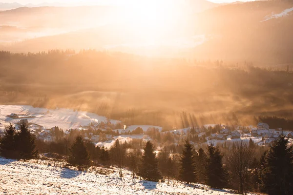 Güneş ışınlarının sabah sisinde geçtiği orman örtüsüyle Polonya 'nın Koniakow köyünün üzerinde gün doğumu. Soğuk bir sabahta nefes kesici bir manzara..