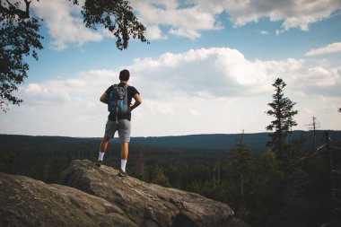 Swarthier 'in tipi bir kayanın tepesinde dikilmiş Zdarske Vrchy' deki bir vadiye bakıyor Çek Cumhuriyeti 'ndeki bir dağ sırasına. Sırt çantalı adam zorlu bir tırmanıştan hoşlanıyor..
