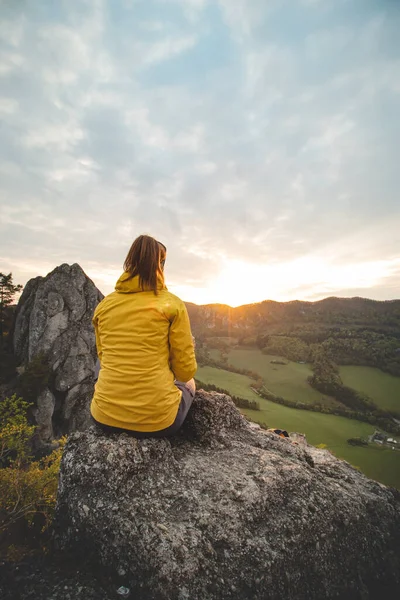 Slovakya 'nın doğusundaki Sulov Kayalıkları' nda gün doğumu. Güzel esmer, sarı ceketli kayanın üzerinde oturuyor. Turuncu ışıkta kayaların olduğu pürüzsüz, el değmemiş bir yer..