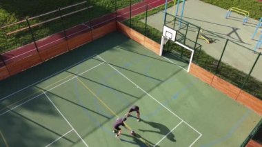 Two friends play one-on-one basketball on an artificial court in summer weather. Active leisure time. Relieve stress by playing. 4k video