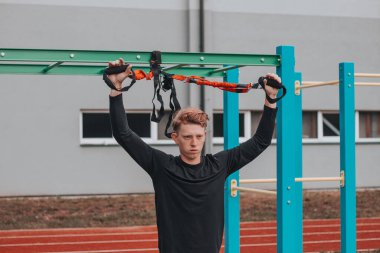 Profesyonel sporcu kollarını, omuzlarını ve göğüs kaslarını Trx fitness kayışlarıyla gerer ve güçlendirir. Azami performans için destek eğitimi.