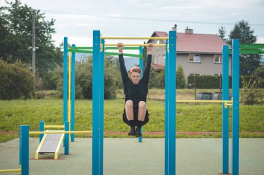Hedef odaklı sarışın çocuk yaz boyunca antrenman sahasında kendi vücudunun gücünü oluşturur. Antrenman trisepsleri, pazılar, omuzlar ve karın kasları. Crosfit egzersiz barfiksleri.