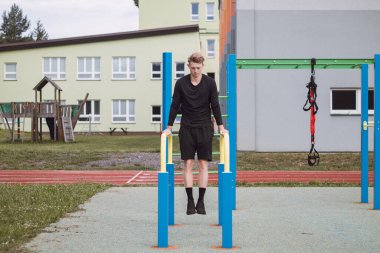 Hedef odaklı sarışın çocuk yaz boyunca antrenman sahasında kendi vücudunun gücünü oluşturur. Antrenman trisepsleri, pazılar, omuzlar ve karın kasları.