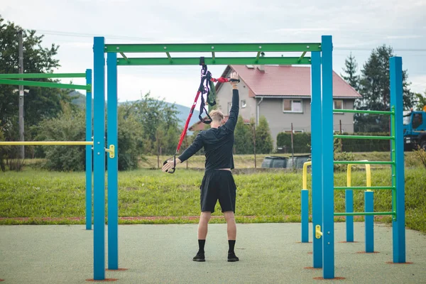 professional athlete stretches and strengthens his arms, shoulders, pectoral muscles and back muscles around the spine with Trx fitness straps. Support training for maximum performance.