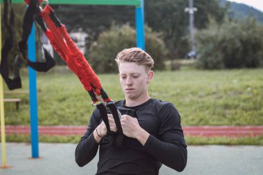 Profesyonel sporcu kollarını, omuzlarını ve göğüs kaslarını trx fitness kayışlarıyla gerer ve güçlendirir. Maksimum performans için destek eğitimi. Odaklanmış performans.