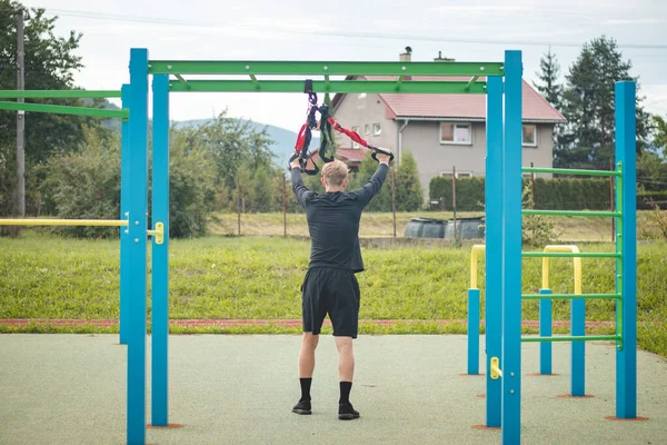 professional athlete stretches and strengthens his arms, shoulders, pectoral muscles and back muscles around the spine with Trx fitness straps. Support training for maximum performance.