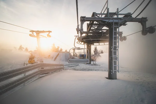 Sunrise breaking through the thick white fog at the top of Vuokatti Hill, a ski resort in Vuokatti, Finland. A view of the frozen chairlift. The Scandinavian experience of winter.