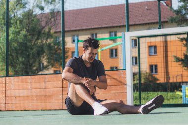 Siyah saçlı sporcu, açık hava sahasında güneşin altında sıkı bir idmandan sonra dinleniyor. Yerde oturan yorgun bir sporcu..