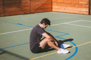 Siyah saçlı sporcu, açık hava sahasında güneşin altında sıkı bir idmandan sonra dinleniyor. Yerde oturan yorgun bir sporcu..
