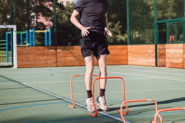 Spor giyimli sarışın çocuk vücut dinamiklerini geliştirmek için kırmızı engellerin üzerinden atlıyor. Açık hava ortamında poliyometrik eğitim. Yeteneklerini geliştir..
