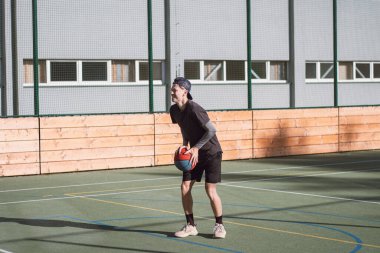 Spor giyim antrenmanındaki sarışın çocuk üç sayılık çizginin arkasından basket atıyor. Açık hava basketbol sahası. Mevsime hazırlanıyorum..