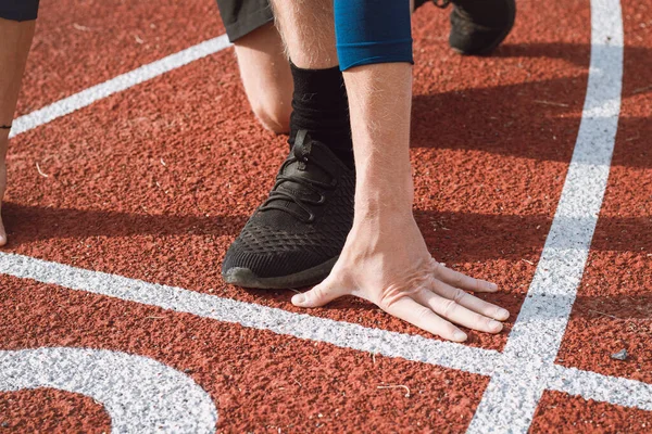 Detail of a professional athlete\'s hand position at the start of a 100m sprint. Outdoor athletics oval.