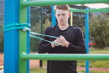 Spor eğitmeni, vücudun üst kısmını sabah spor salonunda genişleticilerin ve lastik bantların yardımıyla çalıştırır. Göğüs ve omuz kasları ısınıyor..