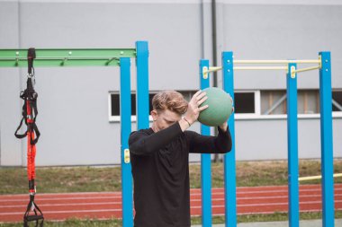 Profesyonel atlet, elinde bir tıp topu ile çömelmiş bir vaziyette duruyor ve ben de onları yere fırlatıyorum. Açık hava idman sahası.