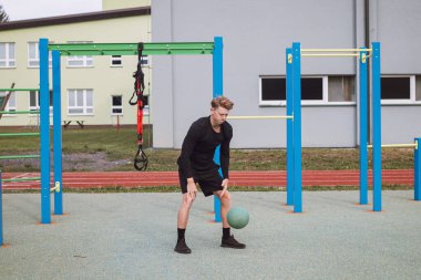 Profesyonel atlet, elinde bir tıp topu ile çömelmiş bir vaziyette duruyor ve ben de onları yere fırlatıyorum. Açık hava idman sahası.