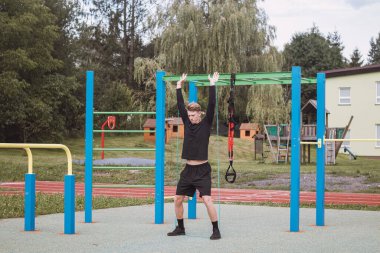 Fitness antrenörü sabahları tüm vücudunu spor salonunda genişletici ve lastik bantlarla çalıştırıyor. Vücudun karmaşık ve büyük kas gruplarının ısınması.