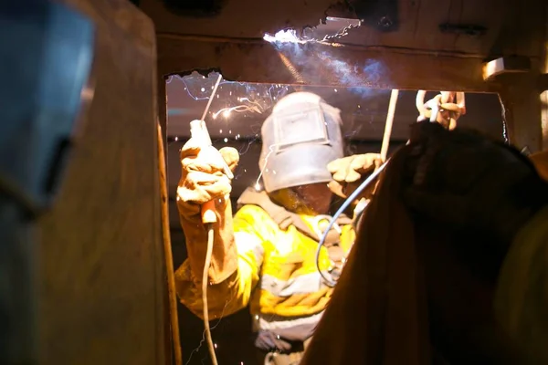 Safety work place rope access welder wearing fully safety uniform fall protection helmet, welding glove harness, commencing welding chute repair in confined space construction mine site Perth Pilbara region Australia