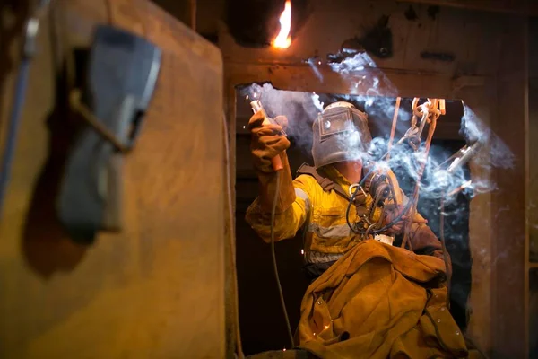 Rope access welder wearing fully safety uniform fall protection helmet, welding glove harness, commencing welding chute repair in confined space construction mine site Perth Pilbara region Australia