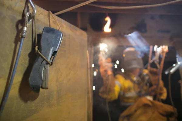 Safety workplace using safety gas testing detector atmosphere while blurry pic of rope access welder wearing fully safety uniform fall protection helmet, welding glove harness, commencing welding, in confined space 