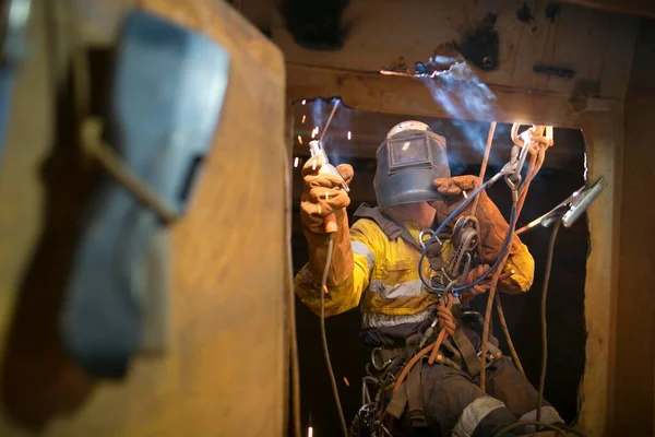 Safety work place rope access welder wearing fully safety uniform fall protection helmet, welding glove harness, commencing welding chute repair in confined space construction mine site Perth Pilbara region Australia
