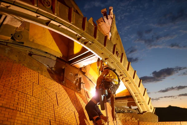 Rope access welder maintenance abseiler wearing fall safety body harness helmet protective gear hanging with rope welding repairing reclaimer wheels bucket construction mine site Perth, Australia sunrise at the background