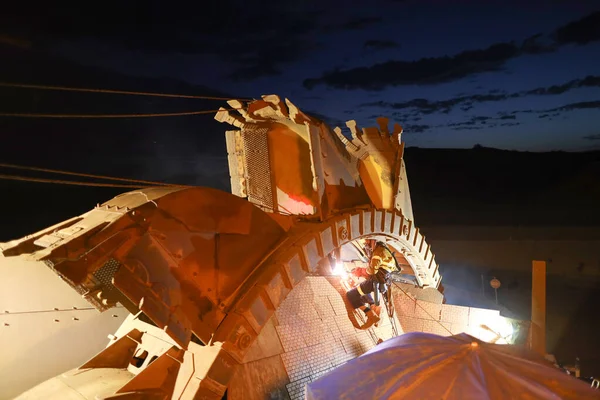 Rope access welder maintenance abseiler wearing fall safety body harness helmet protective gear hanging with rope welding repairing reclaimer wheels bucket construction site Perth, Australia at early morning  