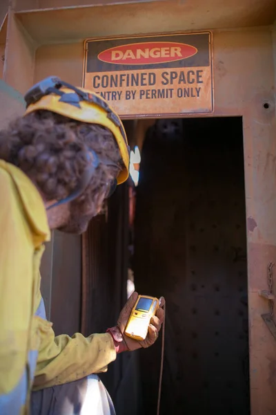 Trained confident constructor worker hand holding gas test leak detector device while commencing safety gas testing atmosphere at main entry and exit on confined space door prior to conducting hot work construction site, Australia   
