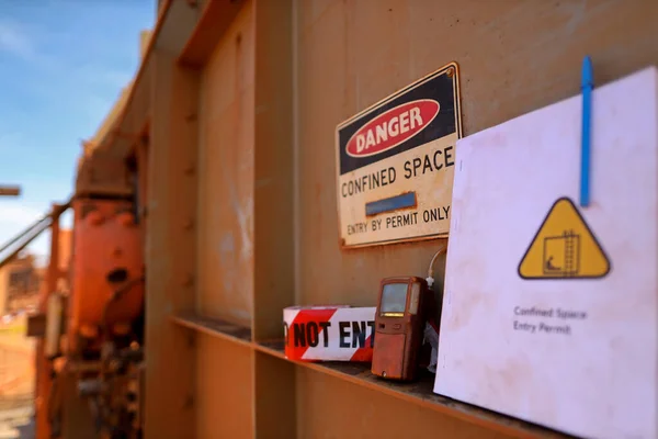 Safety work place confined space permit entry by permit only warning sign and barricade danger tape, caution tape gas leak test atmosphere with defocused permit book template at the foreground construction site