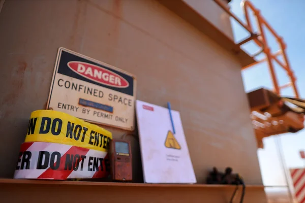 Safety work place warning barricade danger tape, caution tape with defocused gas leak test atmosphere detector at confined space permit at manhole entry and exit door and permit book template at the background construction mine site