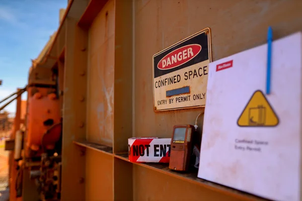 Safety work place warning barricade danger tape with defocused gas leak test atmosphere detector at confined space permit at manhole entry and exit door and permit book template at the background construction mine site