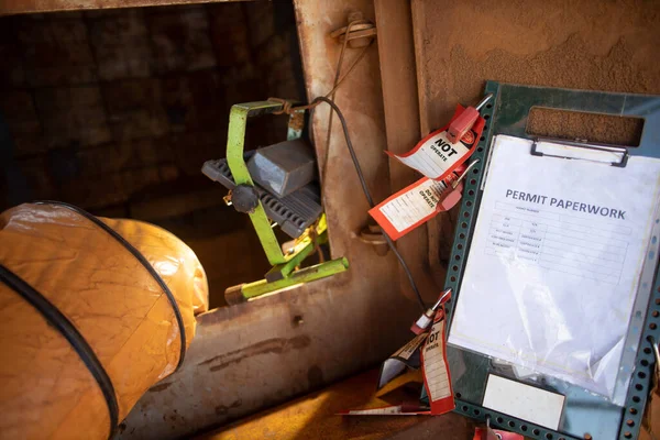 Safety workplace permit to work paper clipping on safety isolation control permit board together with red personal danger locks and tags at confined space entry exit door ventilation fan                   