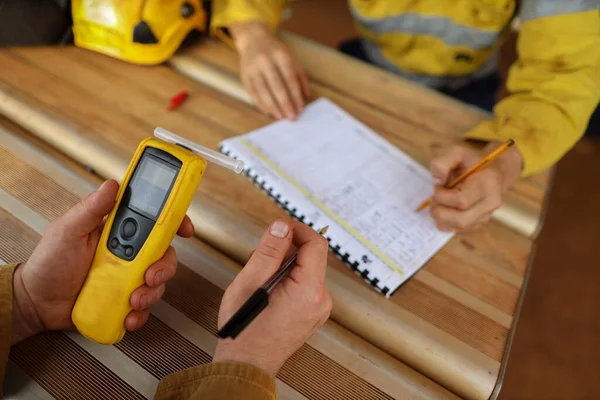 Safety workplace construction miner hand holding checking at breathalyzer breath alcohol testing equipment unit while his friend writing zero alcohol in the blood system on the daily sheet paper prior to work on construction mite site