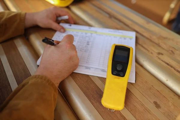Safety work place construction miner writing zero alcohol in the blood body system on the daily sheet prior to work with breathalyzer breath alcohol testing equipment beside him on construction mite site Sydney    
