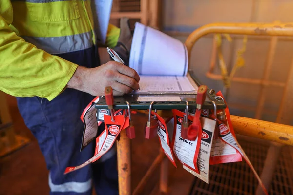 Safety work place pre work checking list personnel red locks attached with danger tag together with safety isolation permit lock box and defocused supervisor permit holder checking co- worker names and signing onto signing sheet