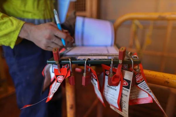 Safety work place pre work checking list personnel red locks attached with danger tag together with safety isolation permit lock box and defocused supervisor permit holder checking co- worker names to ensure their have sign on sheet prior starting