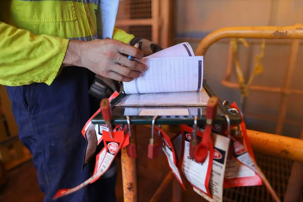 Safety work place miner construction male hands double checking on JHA Job Hazard Analysis sheets before signing working at heights permit to work isolation safety control lock box prior work on opening field construction mine site 