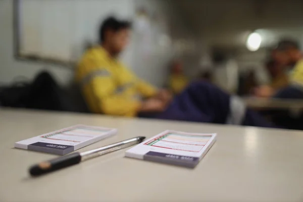 İnşaat güvenliği için kişisel risk değerlendirme kitapçıkları. Beş dakika ara. Arka plandaki sandalyede oturan ve uyanmış üniformalı işçi kıyafetiyle masaya yerleştirilen kalem.   